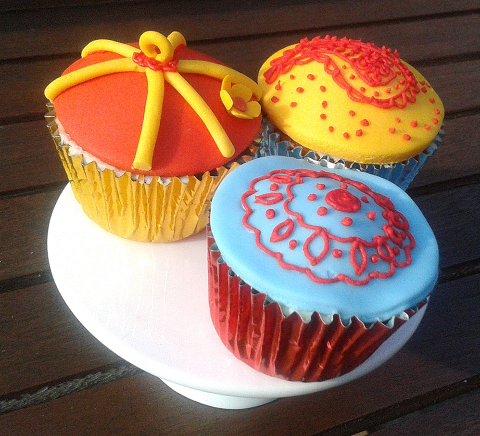 A plate of cupcakes decorated in blue yellow and red. The cupcakes sit on a white plate and are in foil cups.