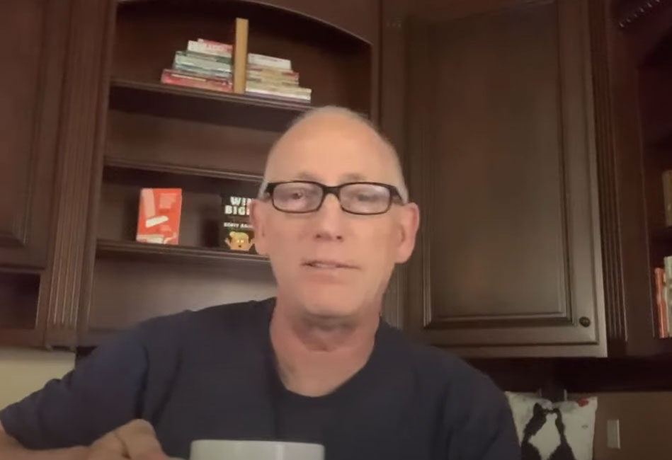 Scott Adams holding a coffee cup and sitting in his kitchen. Behind him are his book Win Bigly and How To Fail At Almost Anything