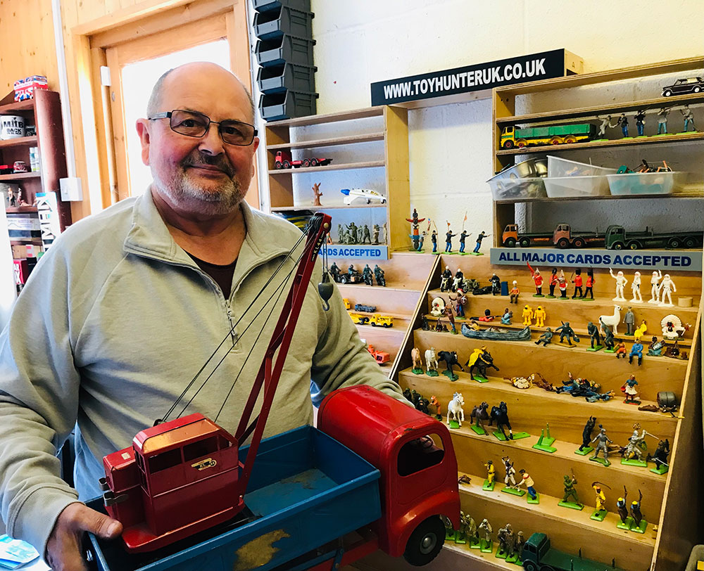 Nick Munford of Toy Hunter stands in front of rows of toy soldiers. He holds a vintage truck in his hands.